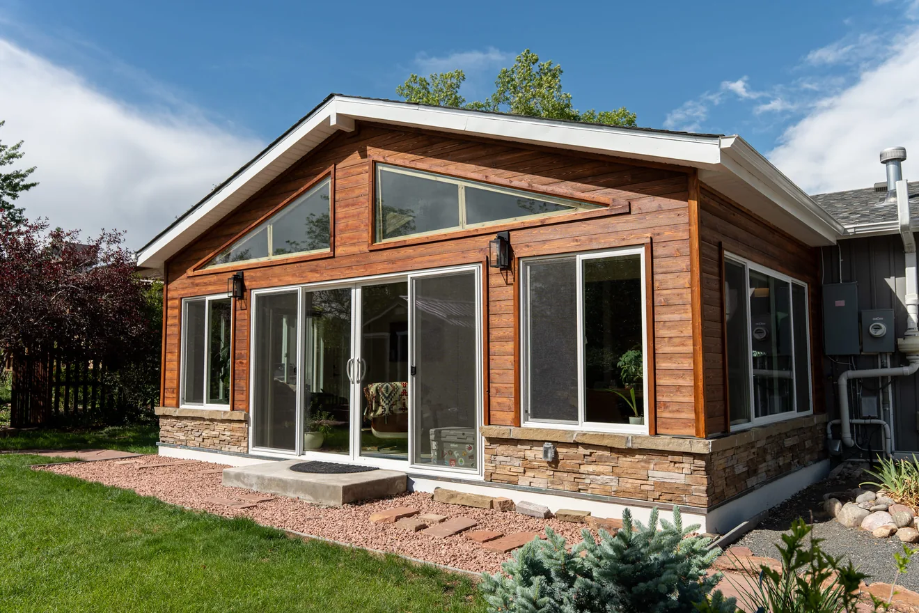 Angled exterior view of the completed sunroom addition with matching siding, windows, and stone base